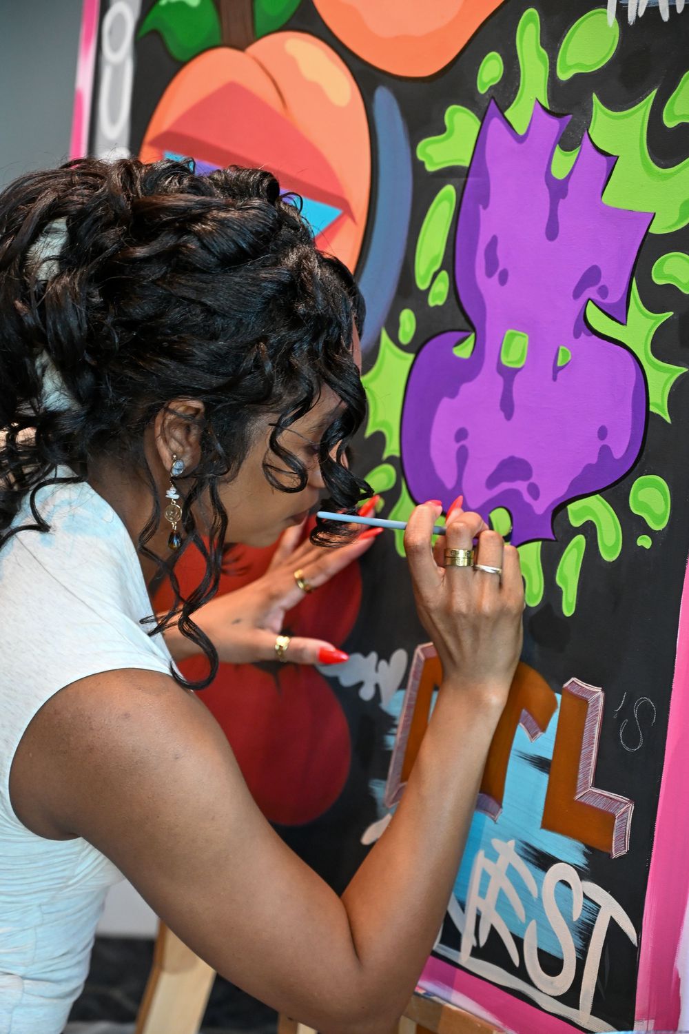 Artist sprays colorful graffiti on a wall with bright neon purple and green dripping paint designs.