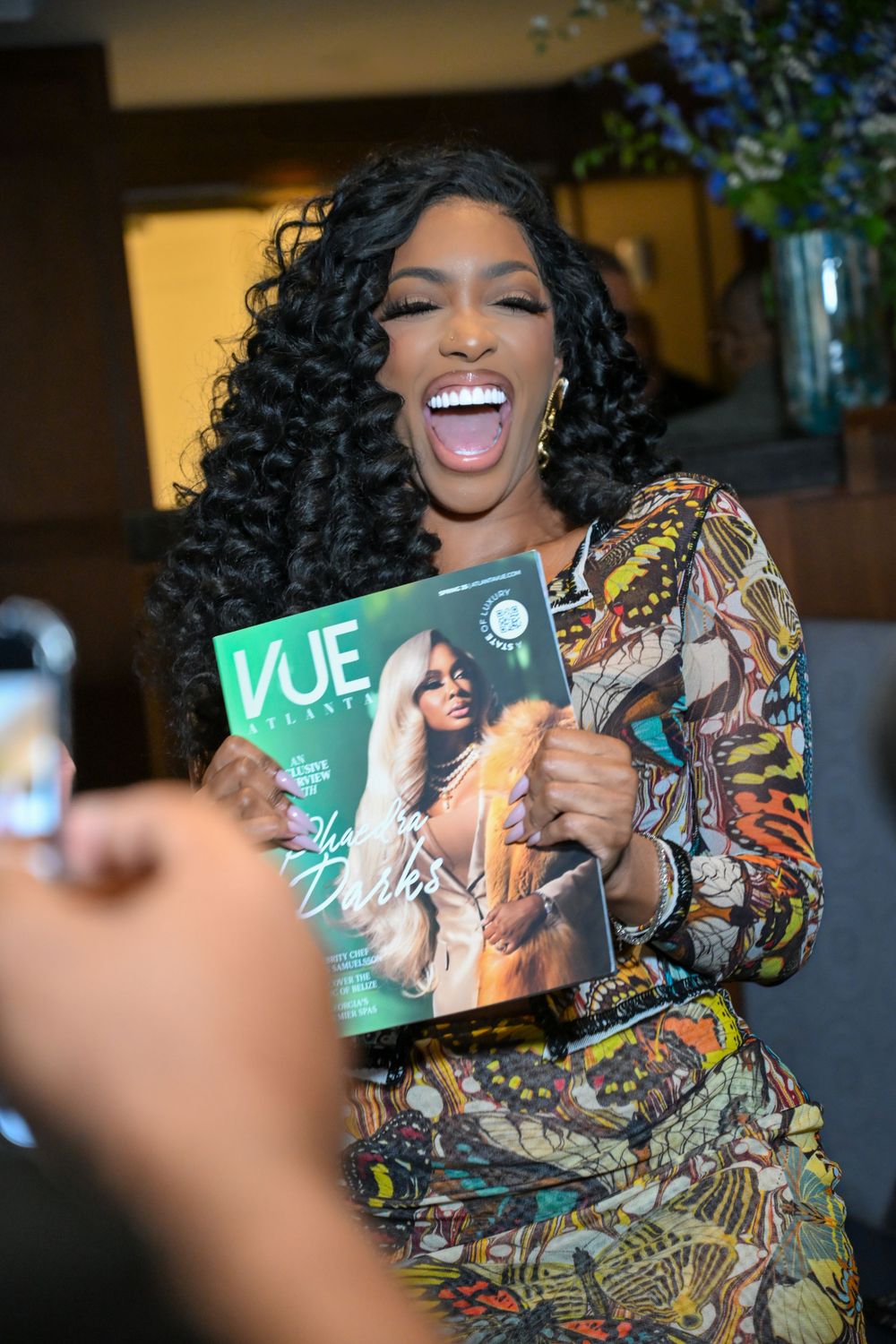 Person in colorful patterned outfit joyfully displaying and posing with VUE magazine across multiple shots.