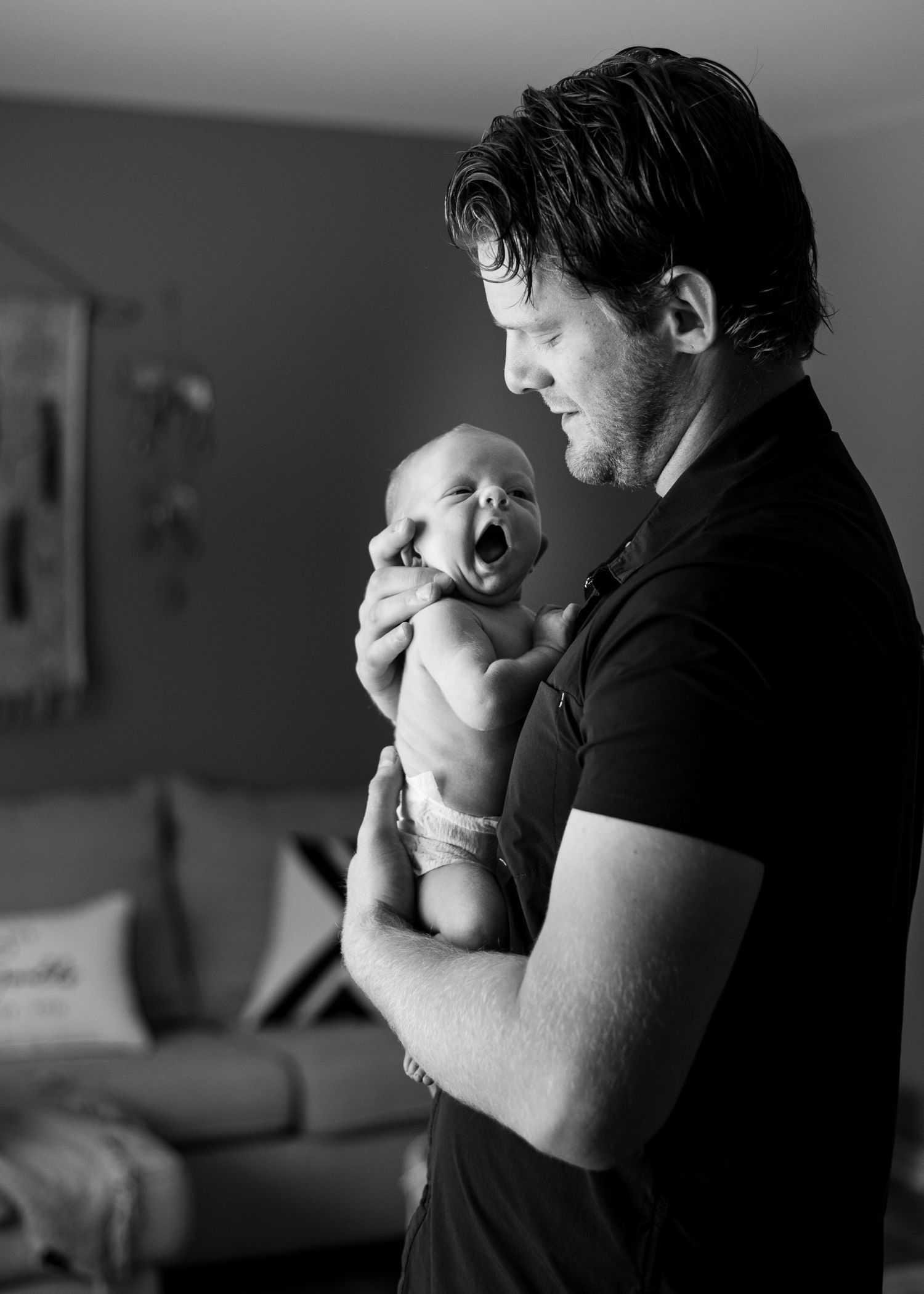 A parent gently holds and looks down at their newborn baby in black and white sequence.