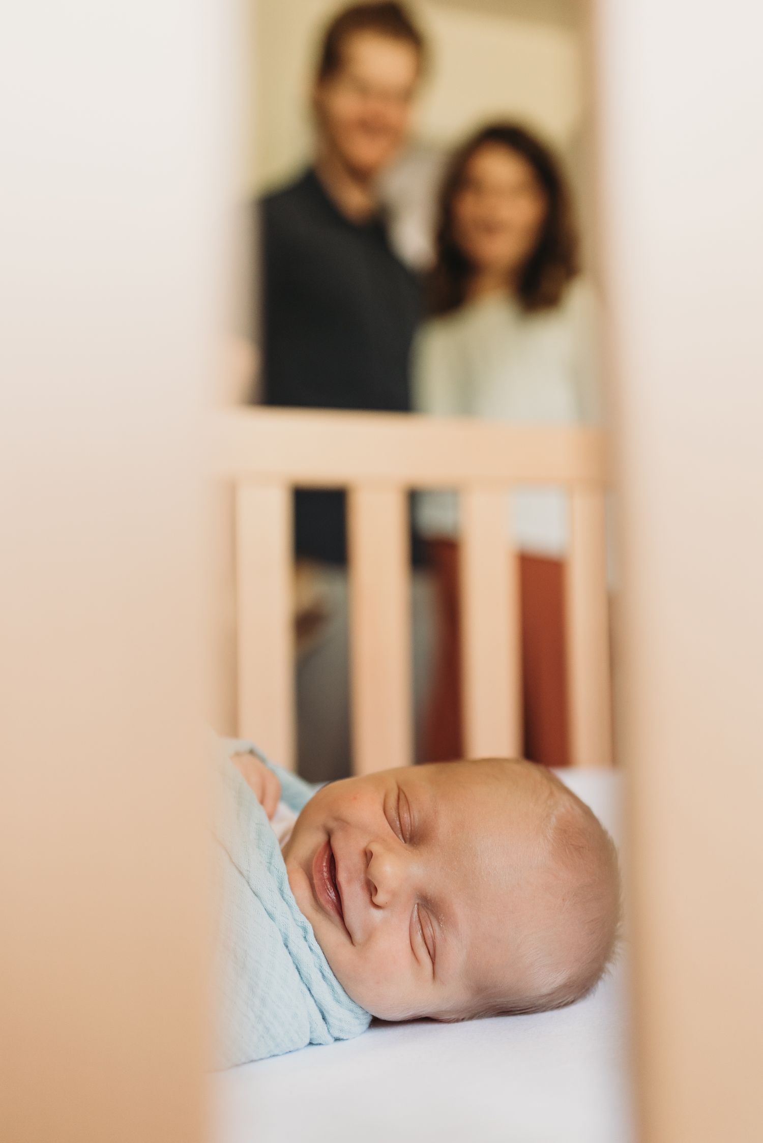 Baby sleeping peacefully in blue swaddle blanket on soft surface with neutral toned background.