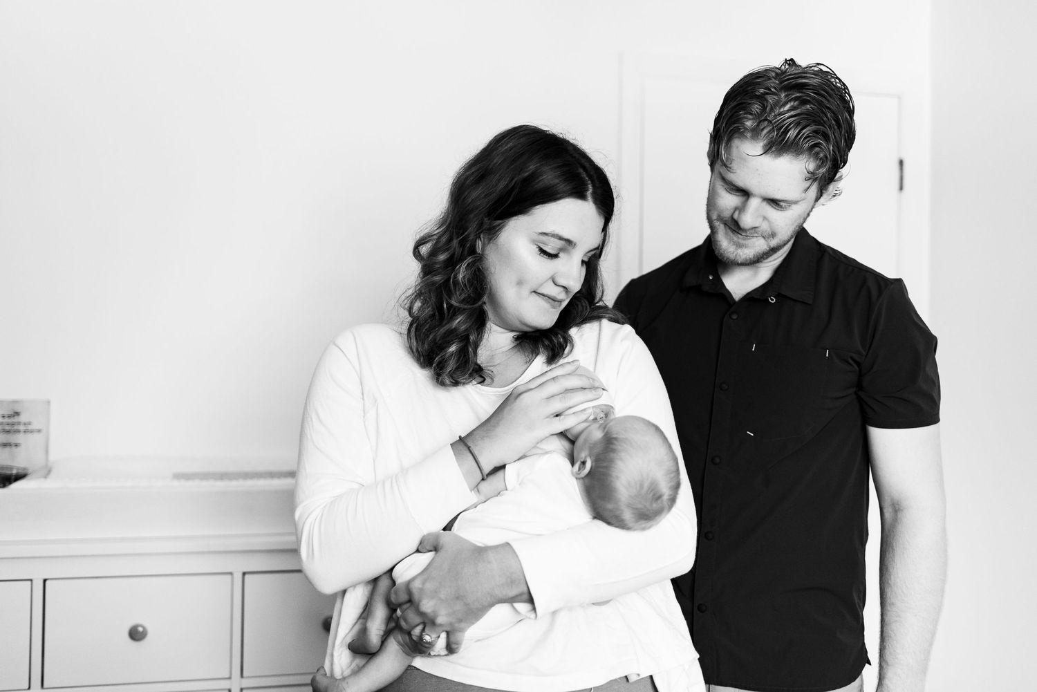 Black and white photo series showing tender moments between mother, father and their newborn baby at home together.