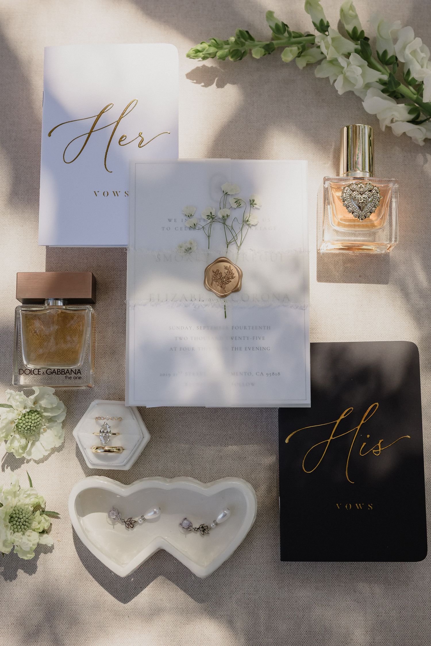 Wedding stationery flatlay with vow books, perfume bottles and heart-shaped trinket dishes.