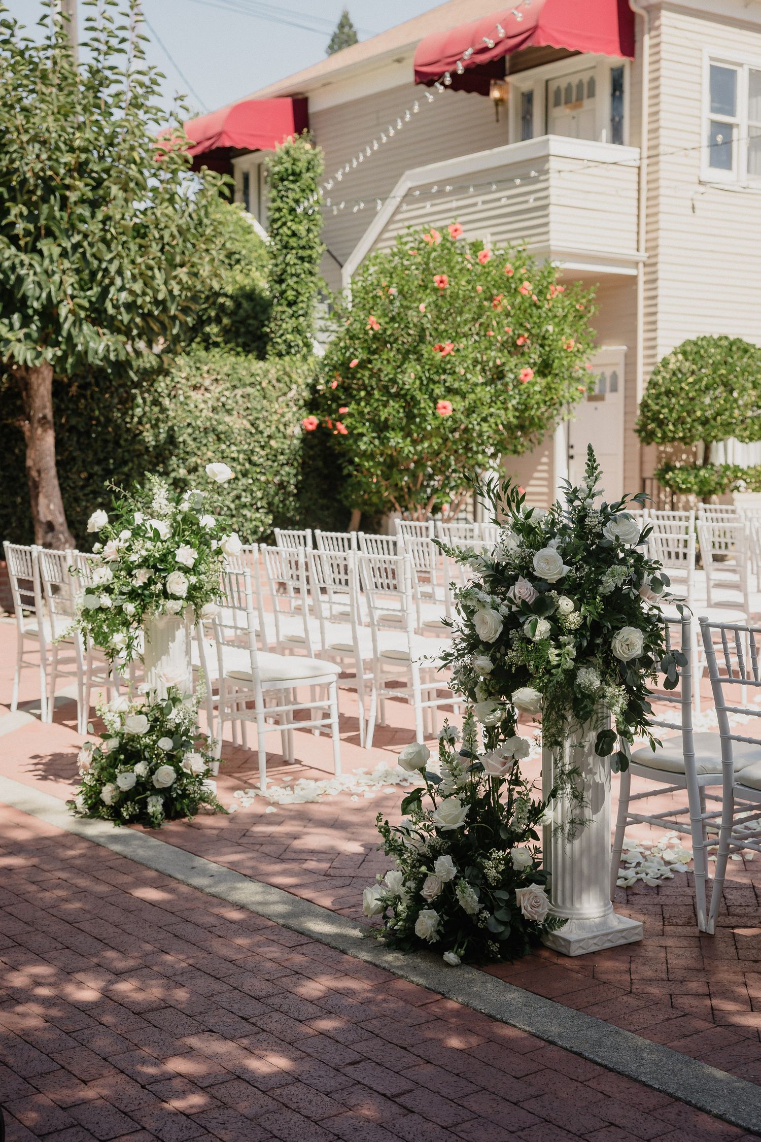Outdoor wedding ceremony setup with white chairs and floral arrangements along brick pathway.