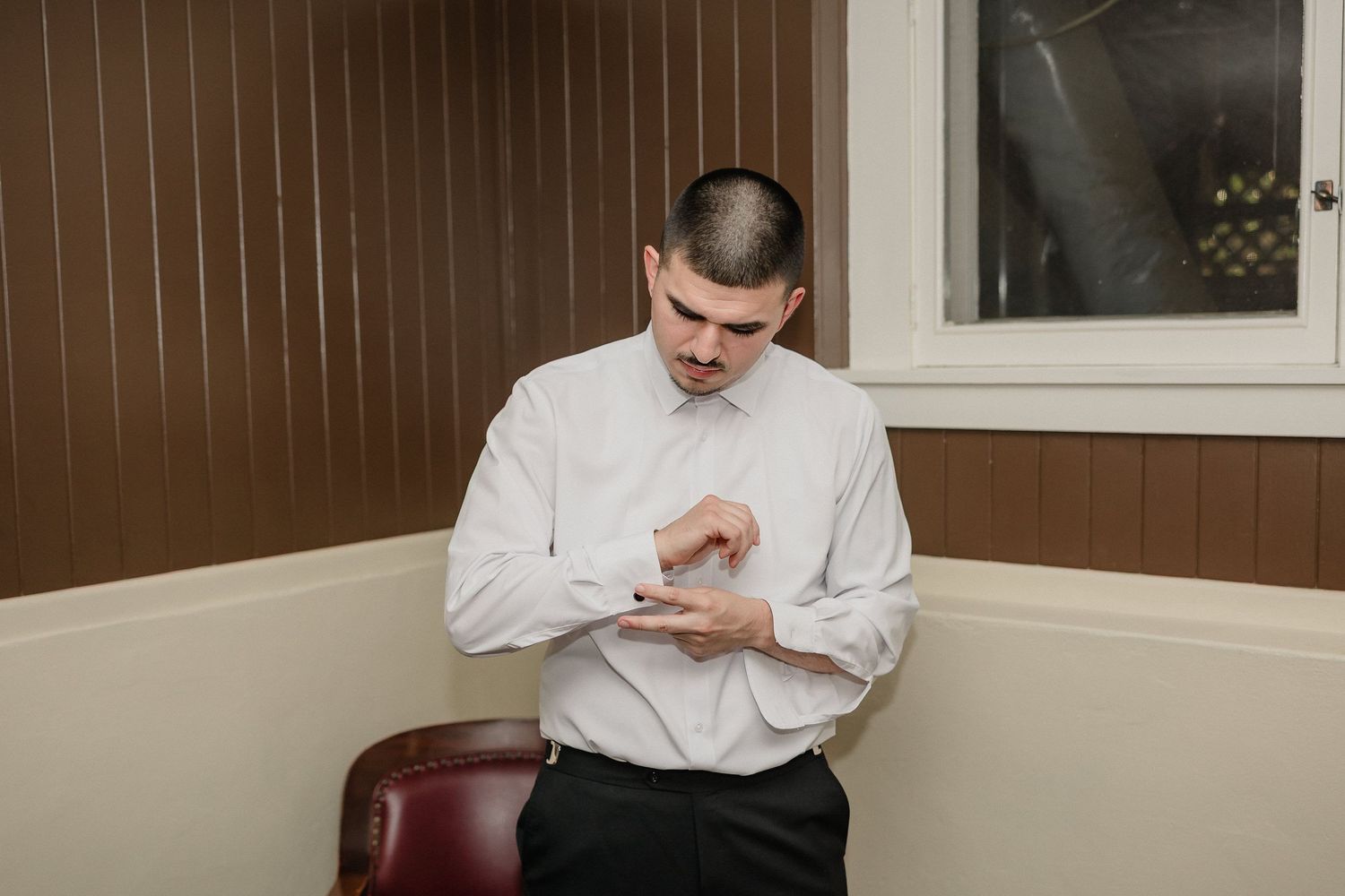 Groom checking time on watch while sitting in leather chair.