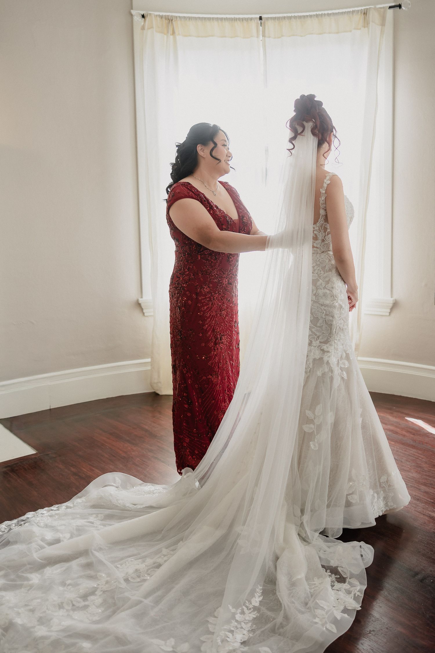 Elegant lace wedding dress with long train being arranged in naturally lit room.