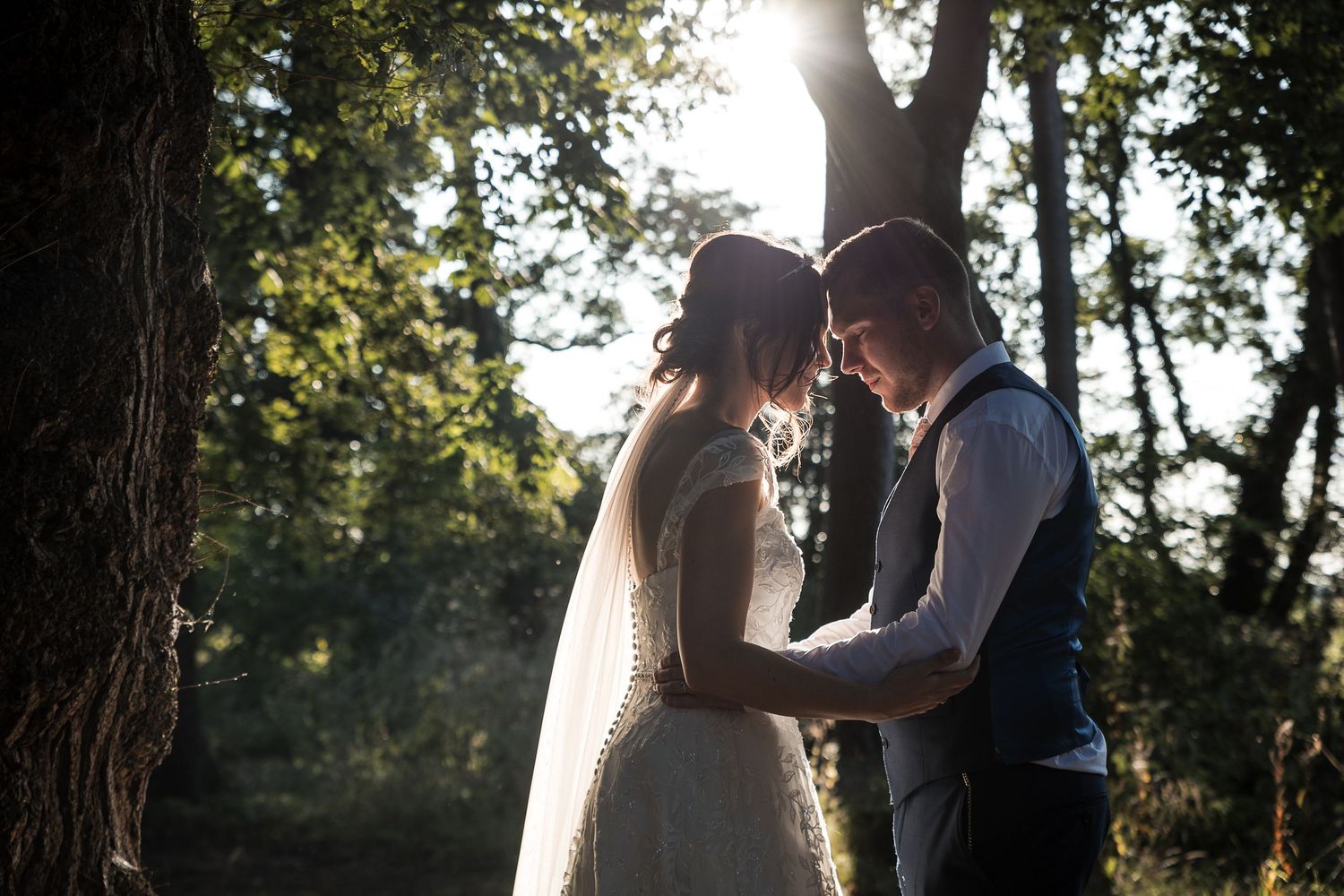 Couple sharing a romantic golden hour wedding moment beneath sunlit trees at Kelham House