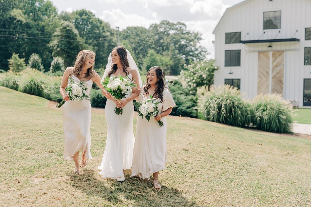 Elegant outdoor wedding celebration showing guests in white and cream dresses on a lush green hillside.