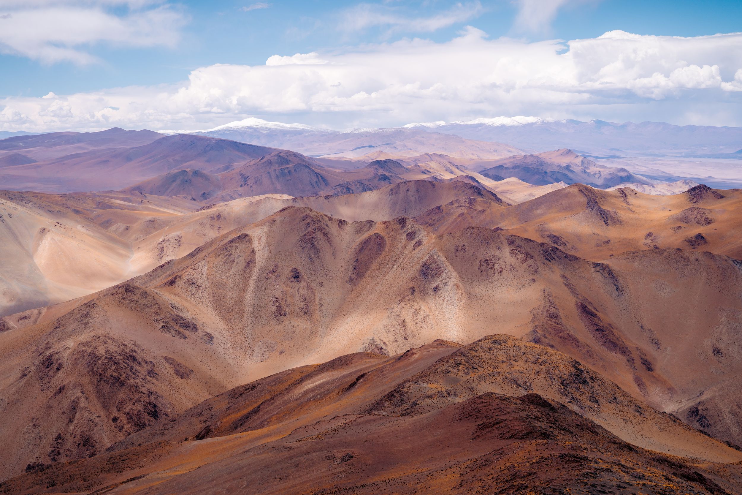 Panoramic view of rugged brown mountain ranges in the desert stretching across the horizon under a bright blue sky.