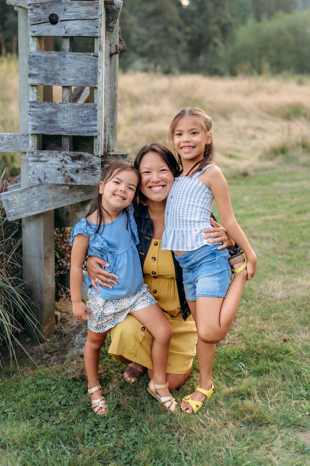 Three people posing by a rustic wooden post in summer attire.