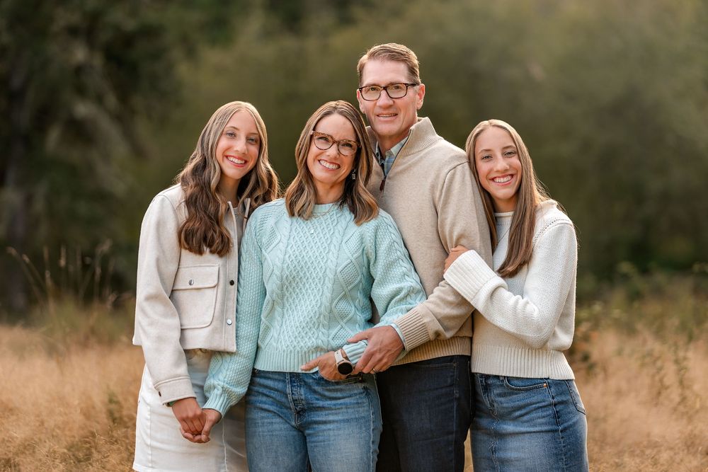 A group of four people in neutral colored sweaters posing in a field.
