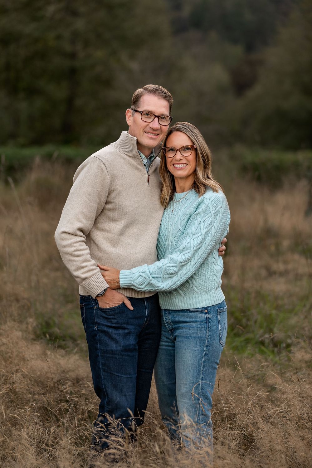 A couple in cozy sweaters embracing in a field during golden hour.