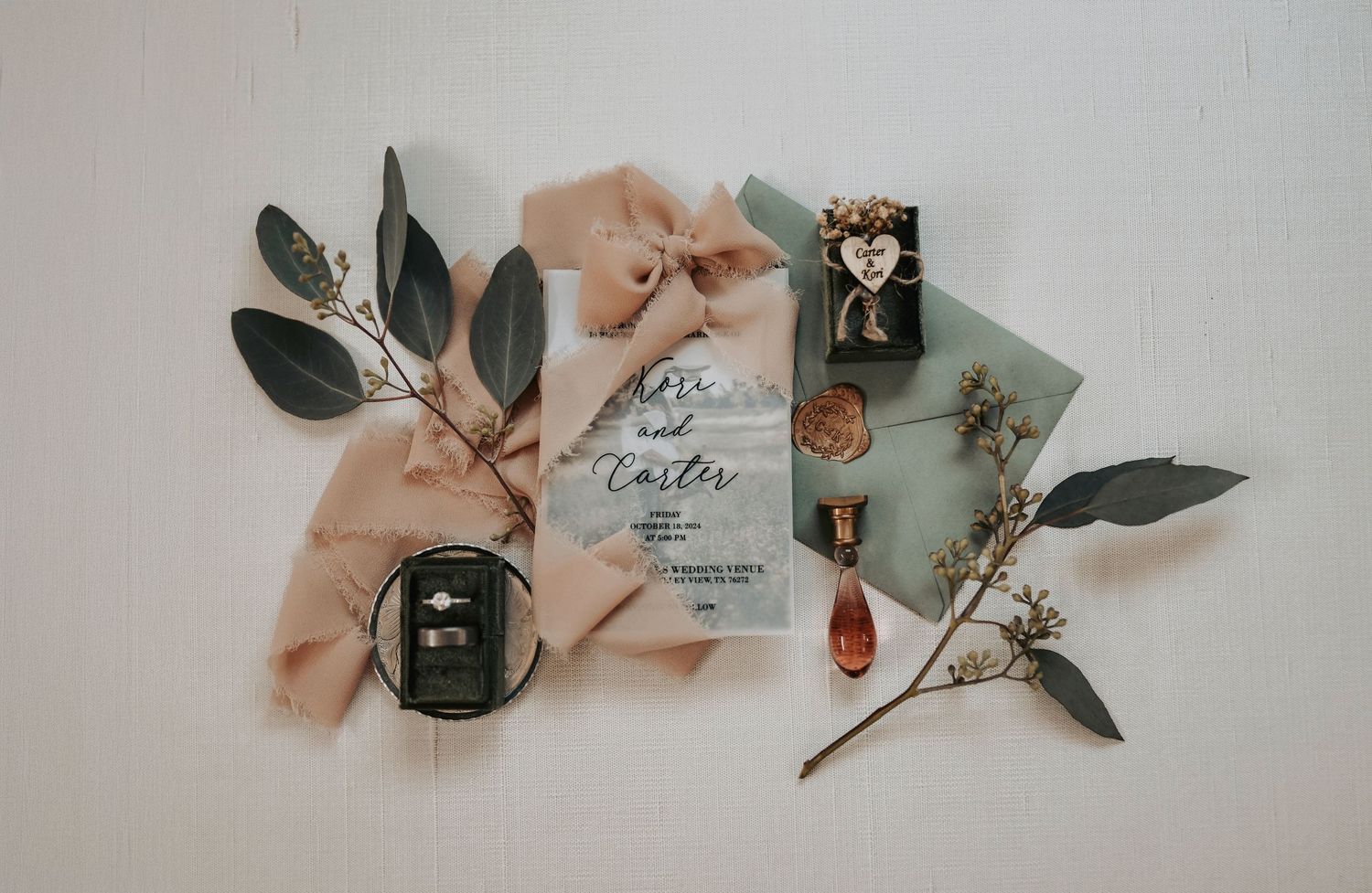 a romantic flat lay of a wedding invitation wrapped in ribbon, surrounded by greenery