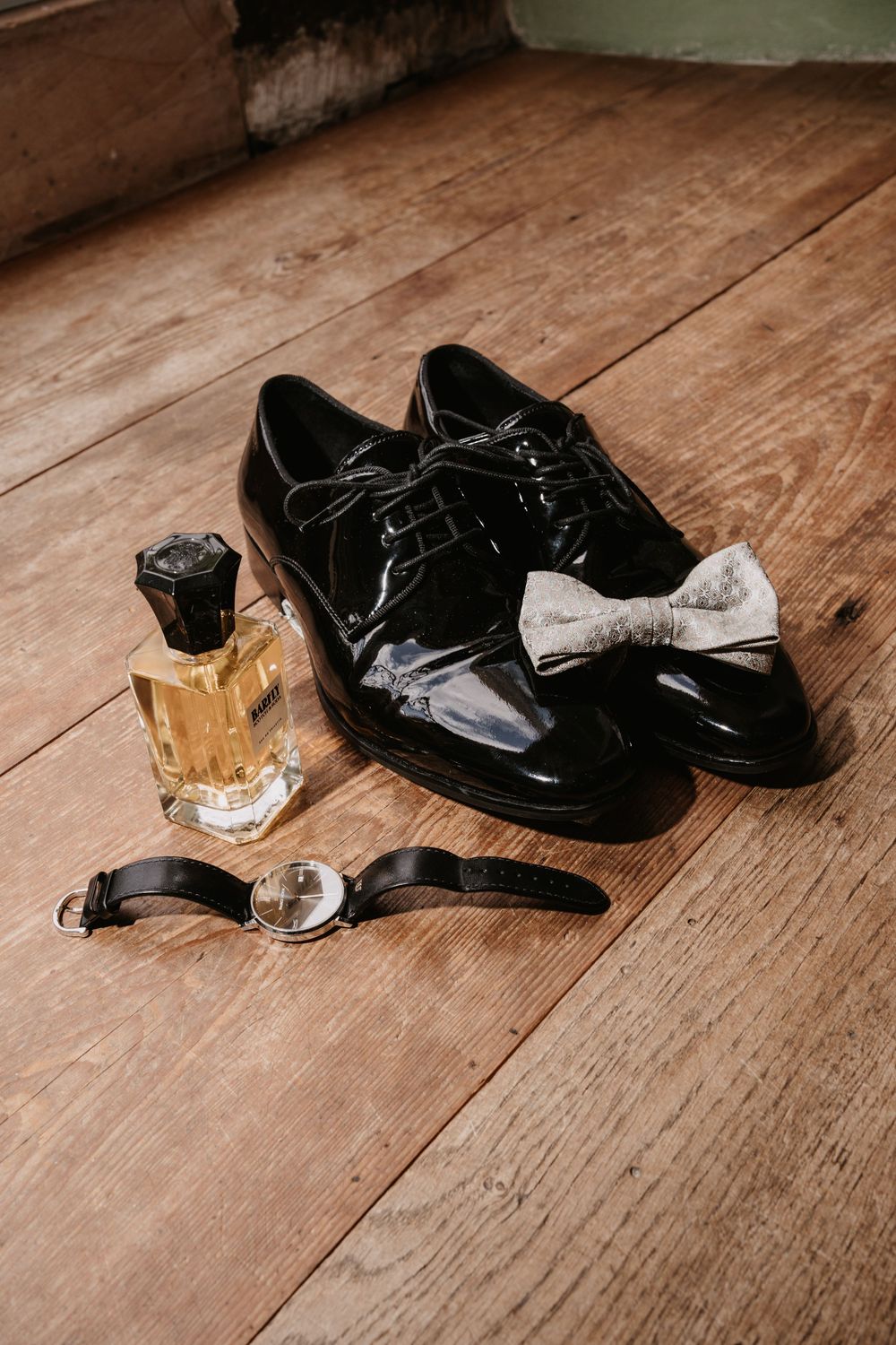 Black formal shoes and accessories arranged on rustic wooden floorboards in preparation for a wedding.