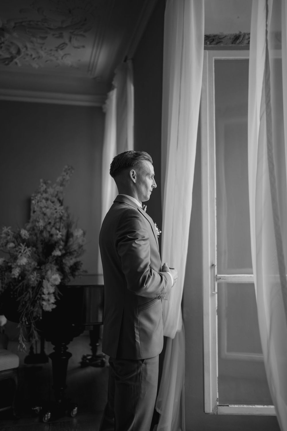 A black and white photo series showing a person in a suit checking their watch near a window with flowing curtains.