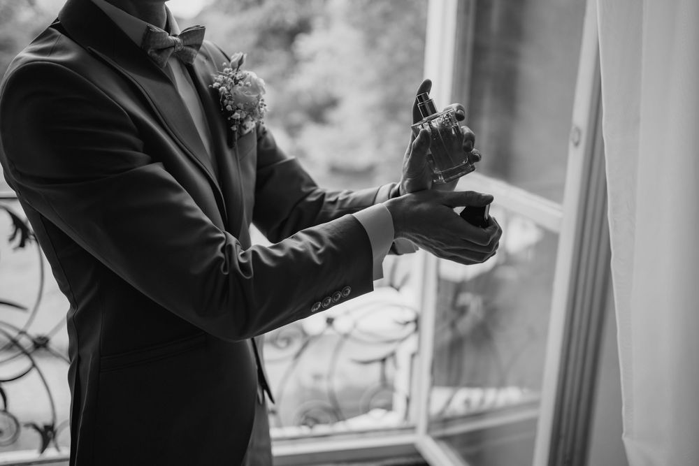 Black and white wedding photo showing a couple dancing together in formal attire by a sunlit window.