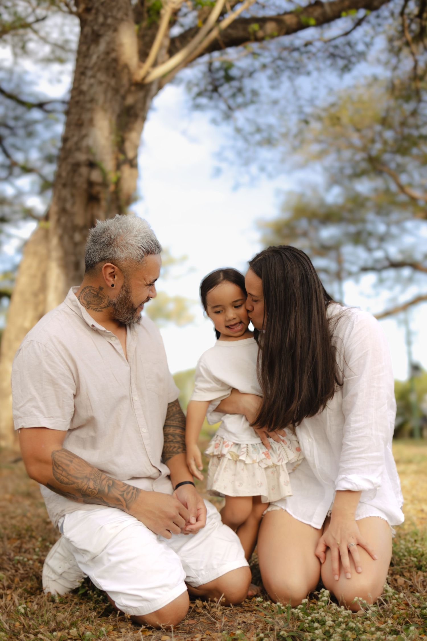 Family members sitting together on grass under trees wearing coordinated white outfits.