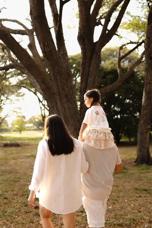 Family walking together through a grove of large trees in matching white outfits.