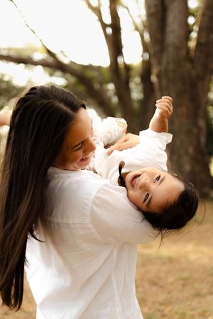 Playful interaction between parent and child laughing together against a backdrop of trees.