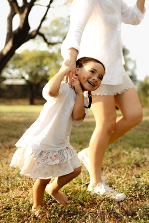 A small child in white dress twirling and playing in a park during sunset.