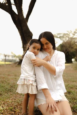 A tender embrace between parent and child outdoors under large trees.
