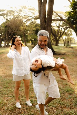 A family playing and laughing together in a park with everyone dressed in white.