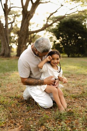An intimate moment shared between family members sitting on grass under trees.