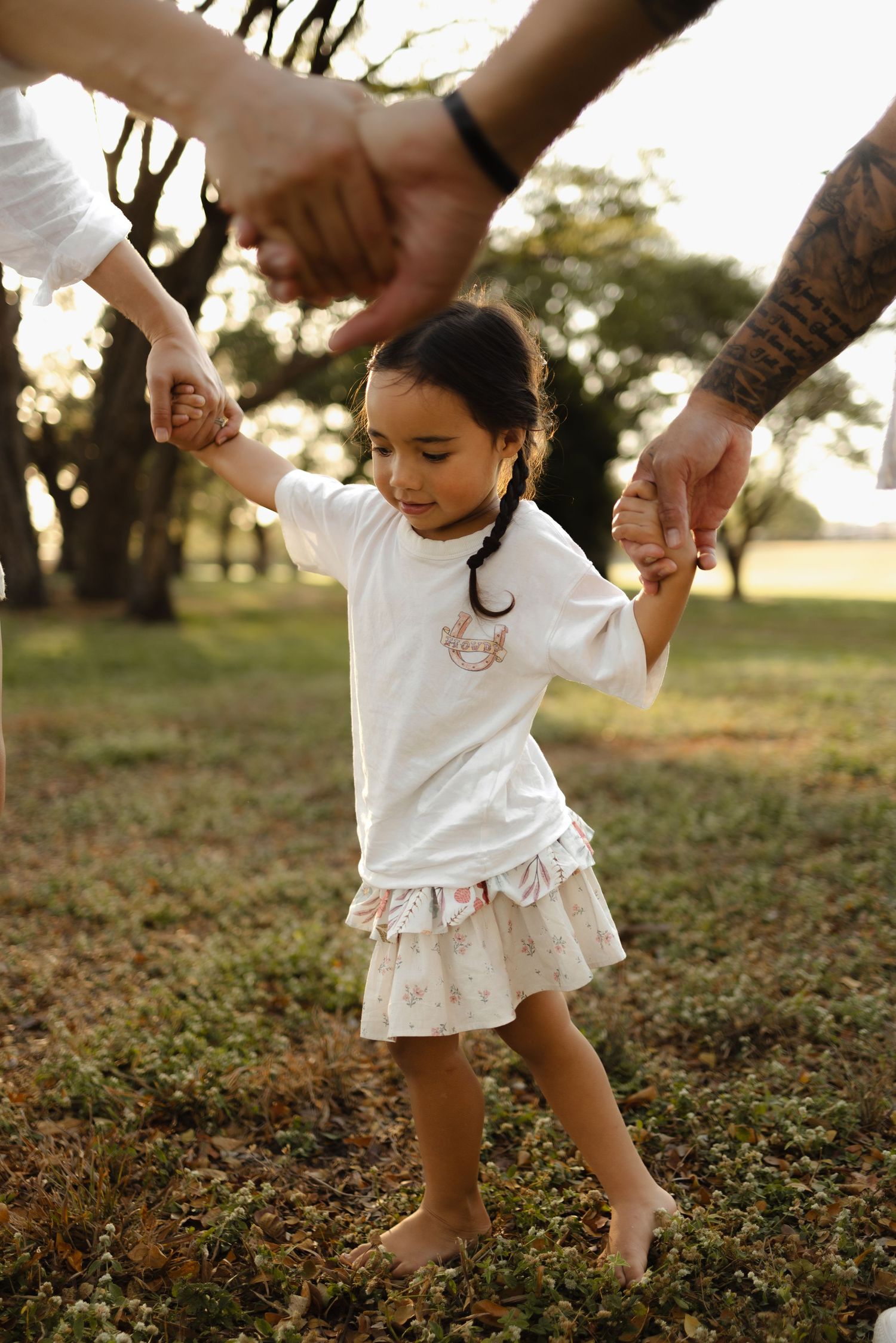 A child holding hands with parents while walking through a park at sunset.