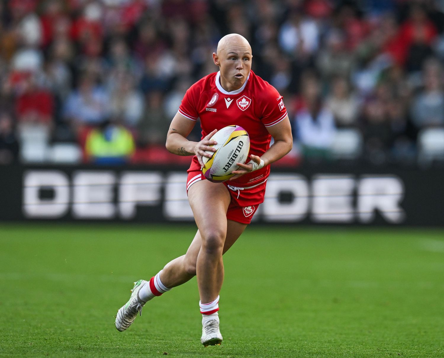 Rugby player in red jersey sprints across field while carrying ball during competitive match.