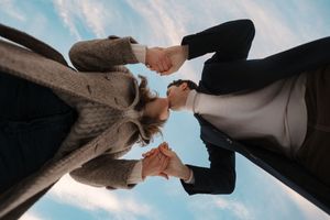 Low-angle view of two people holding hands against a blue sky, symbolizing unity and connection.