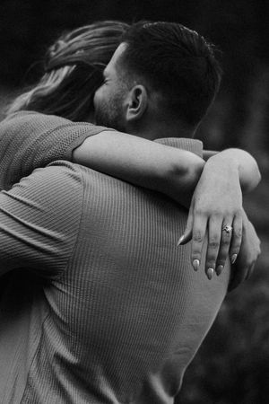 Black and white intimate portrait of a couple embracing, with a ring visible on one hand.