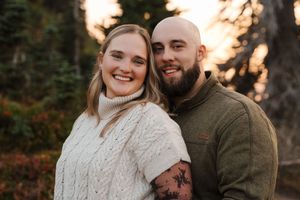 A couple in cozy sweaters embrace during a romantic autumn sunset photoshoot in a forest setting.