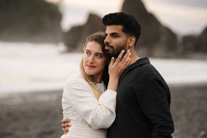 A couple in wedding attire embrace against a moody winter landscape with snow-covered mountains in the background.