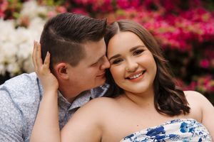 A couple shares an intimate moment among blooming pink and white flowers in a garden setting.