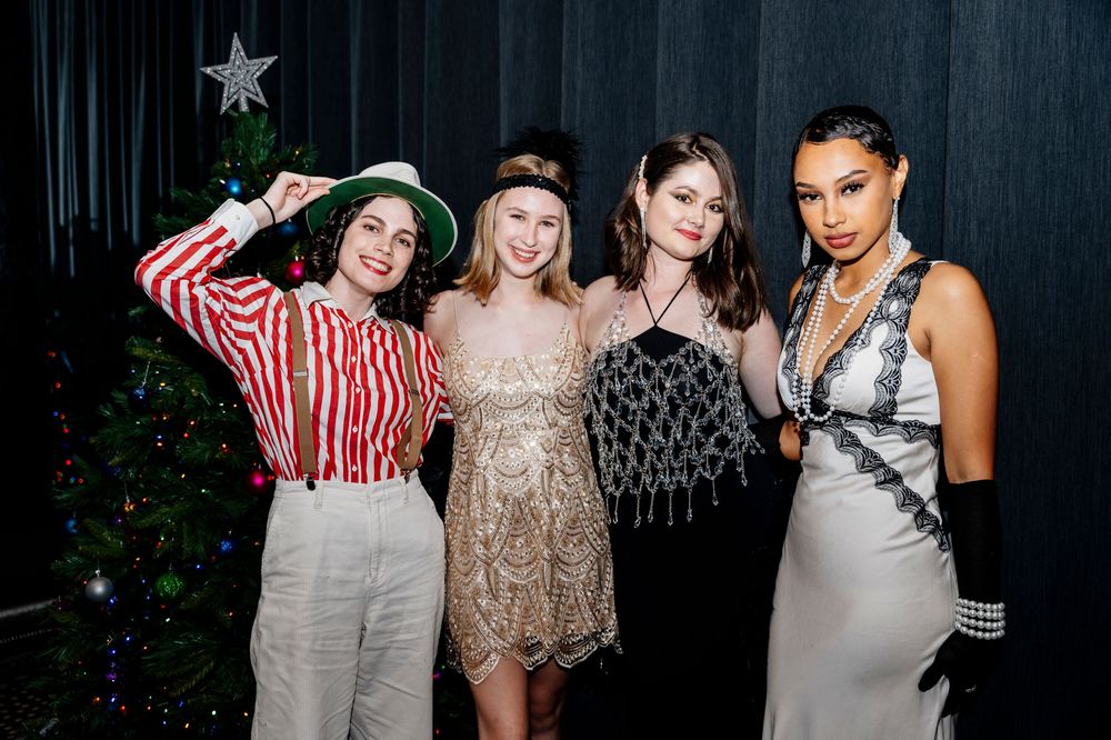 Group of people posing together at a party with dark background and festive decorations.