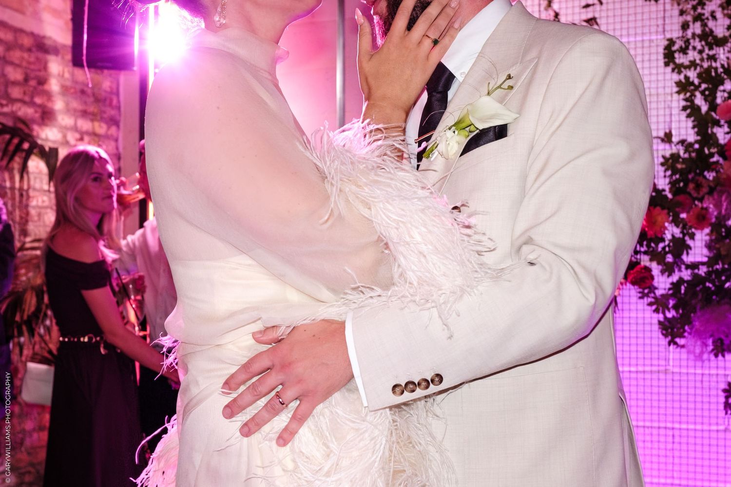 Dance floor at a festive wedding reception with couples dancing under bright pink and purple lighting.