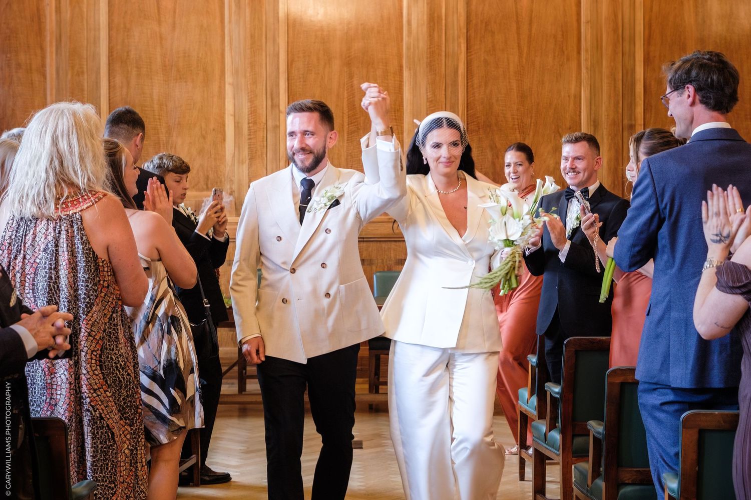Wedding guests dance and celebrate in a rustic wood-paneled reception hall.