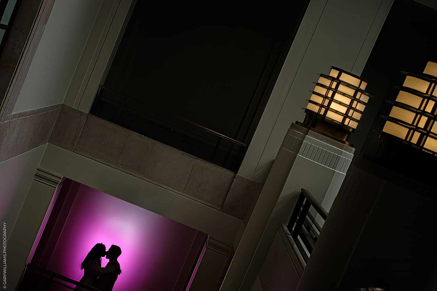 Two figures stand in silhouette against a dramatic purple-lit backdrop in a modern interior space.