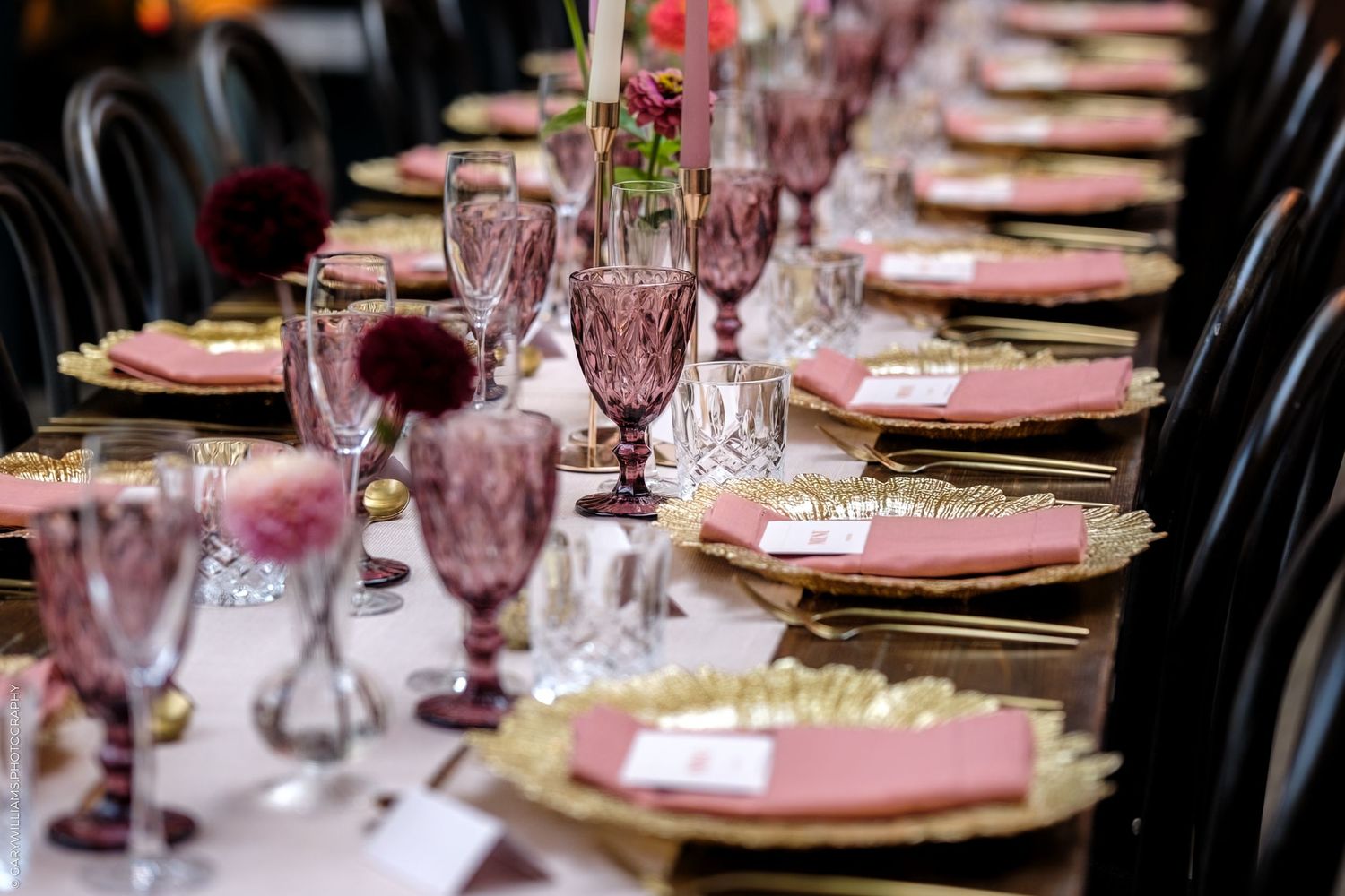 Elegant wedding reception table setting with pink napkins, crystal stemware, and ornate place settings in a formal dining room.