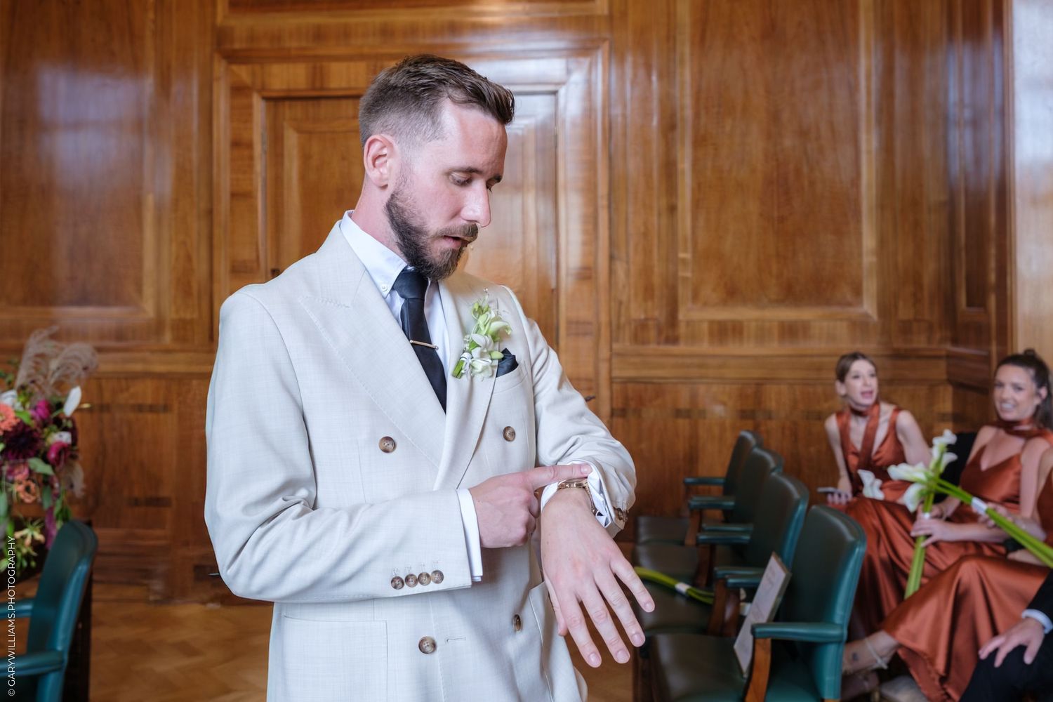 Wedding couple share emotional reactions during ceremony in wood-paneled room with soft lighting.