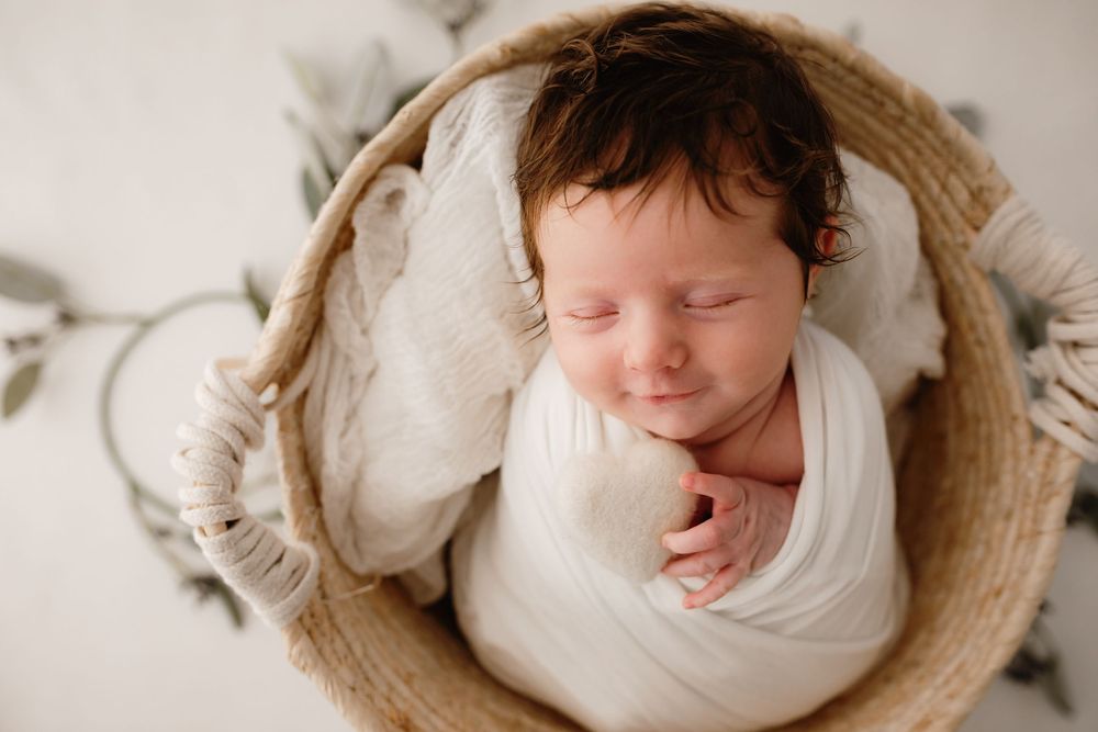 Sleeping newborn wrapped in white swaddle lying in woven basket with soft fabric lining.