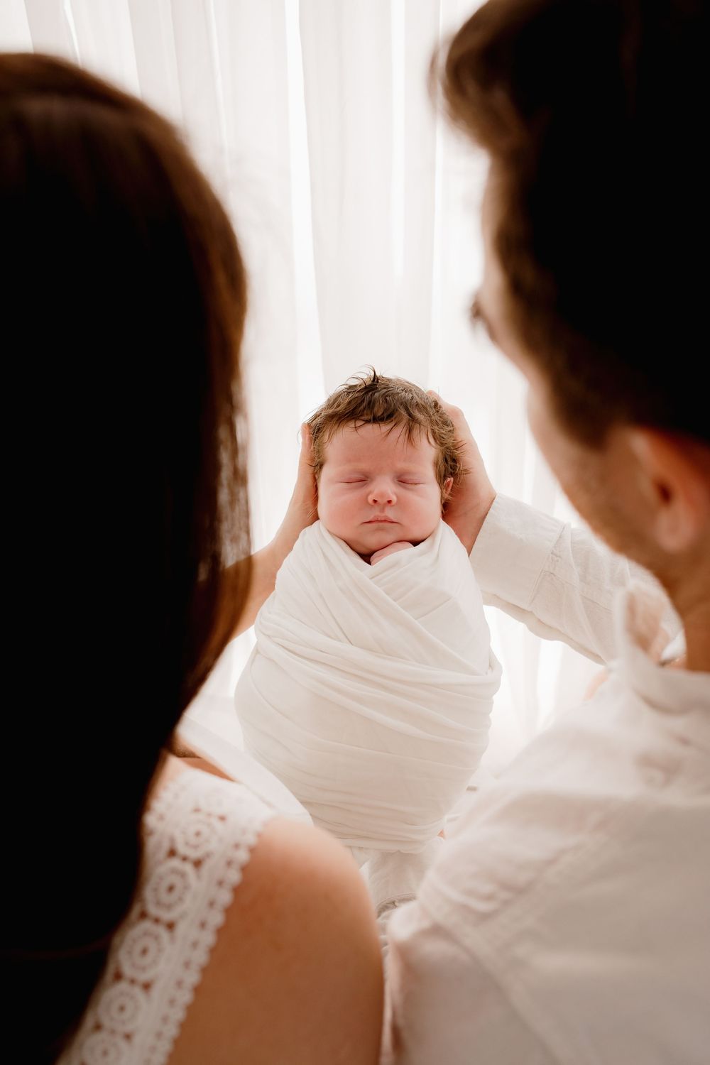 Parents gazing at their swaddled newborn baby in intimate family moment.