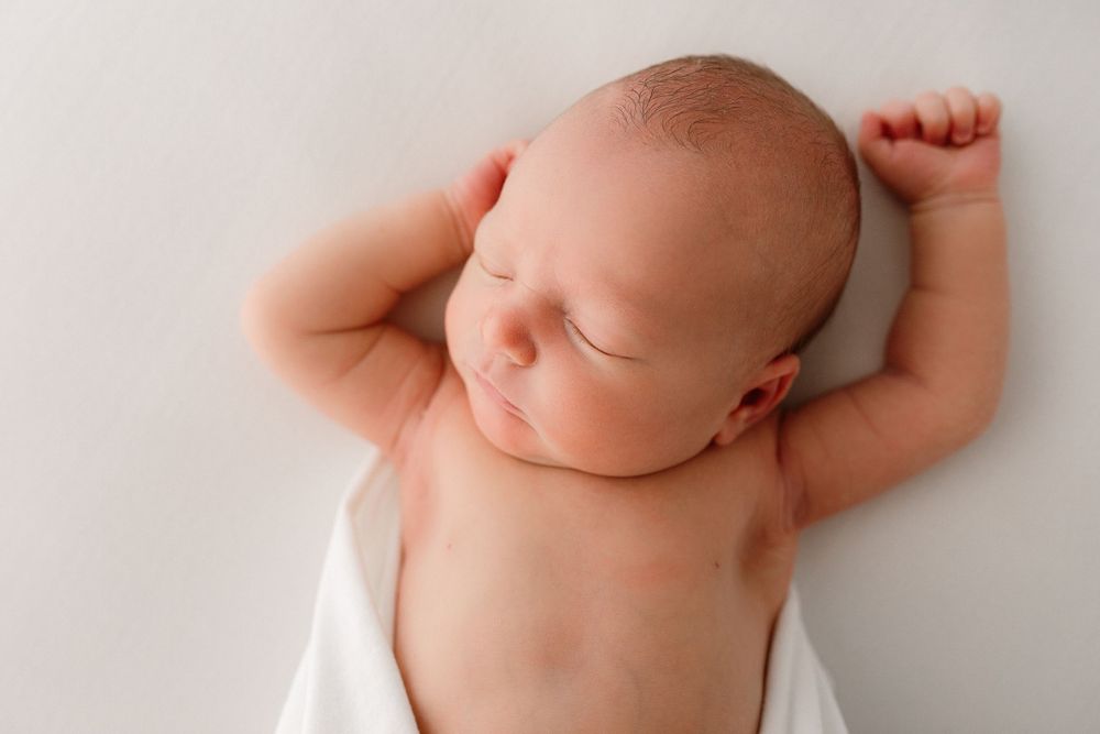 Artistic newborn photography showing peaceful sleeping baby on white backdrop.