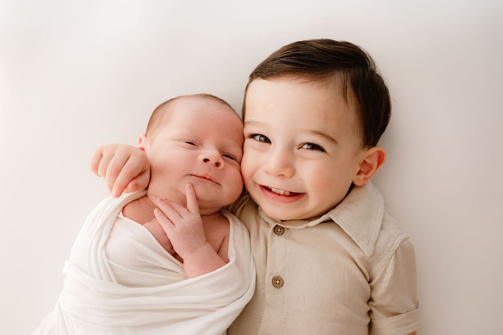 Two young children in light colored clothing sharing a tender moment together on white background.