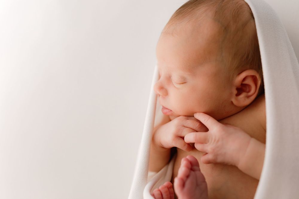 Close-up portraits of sleeping newborn wrapped in soft white fabric.