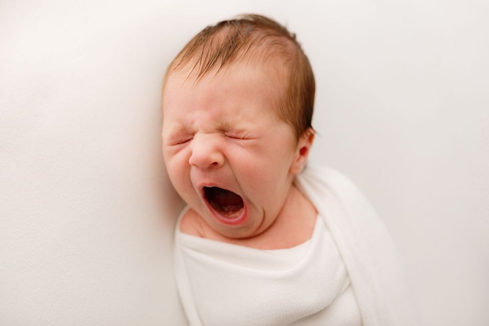 Newborn baby in white wrap making expressive faces during professional photo session.