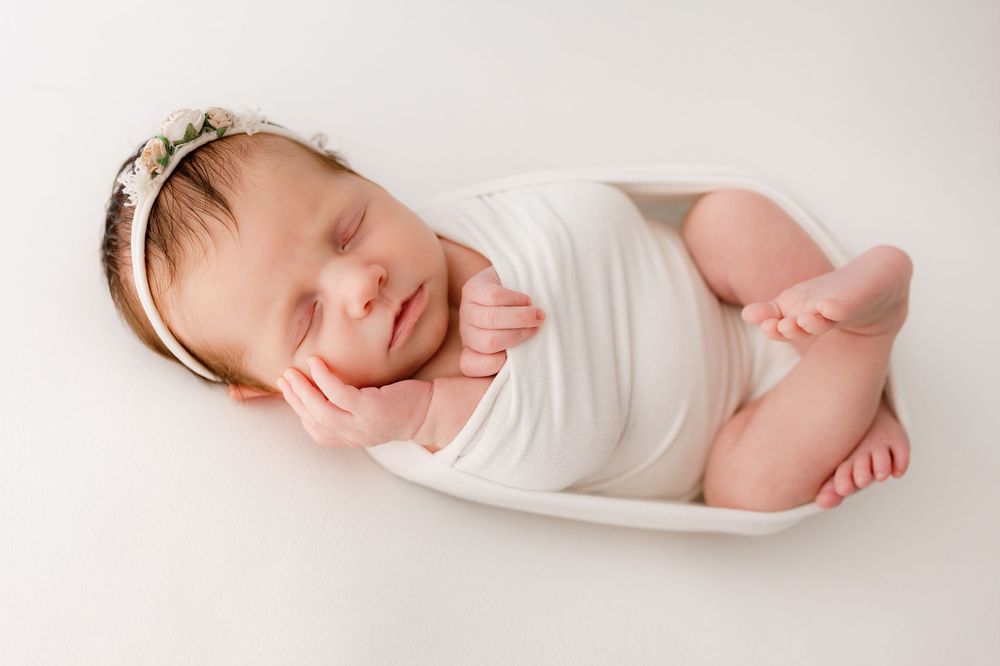 Peaceful sleeping newborn wrapped in white fabric on light background.
