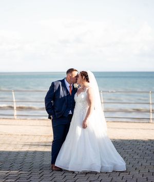 A romantic wedding couple shares an intimate moment on a beach boardwalk with the ocean in the background.
