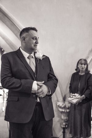 Men in black suits engage in candid moments during a formal event under white arched ceilings.