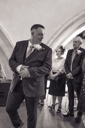 Guests in formal attire mingle and converse during an indoor social gathering with vaulted white ceilings.