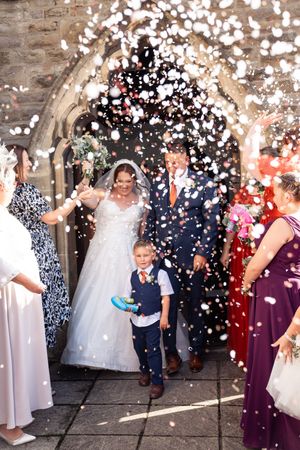 Wedding guests celebrating and throwing white confetti during the outdoor festivities against a stone wall backdrop.